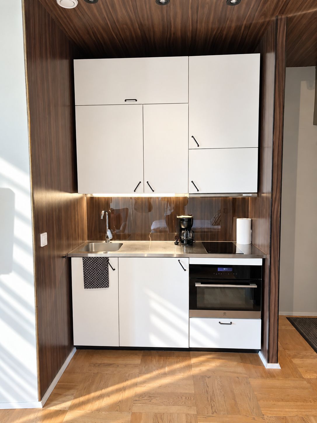 A compact kitchen with white cabinets, a sink, a coffee maker, and an oven.