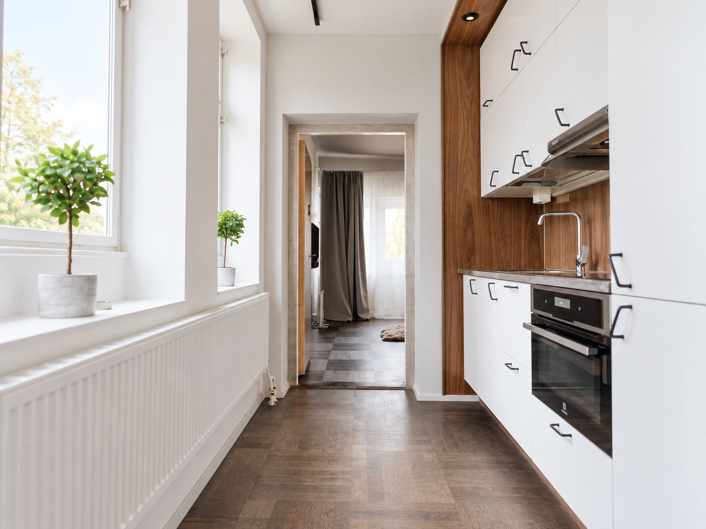 Una cocina moderna con armarios blancos y una pared decorativa de madera, una planta en maceta junto a la ventana, y vista al área de estar contigua.