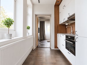 Een moderne keuken met witte kastjes en een houten accentmuur, een potplant bij het raam en uitzicht op de aangrenzende woonkamer.