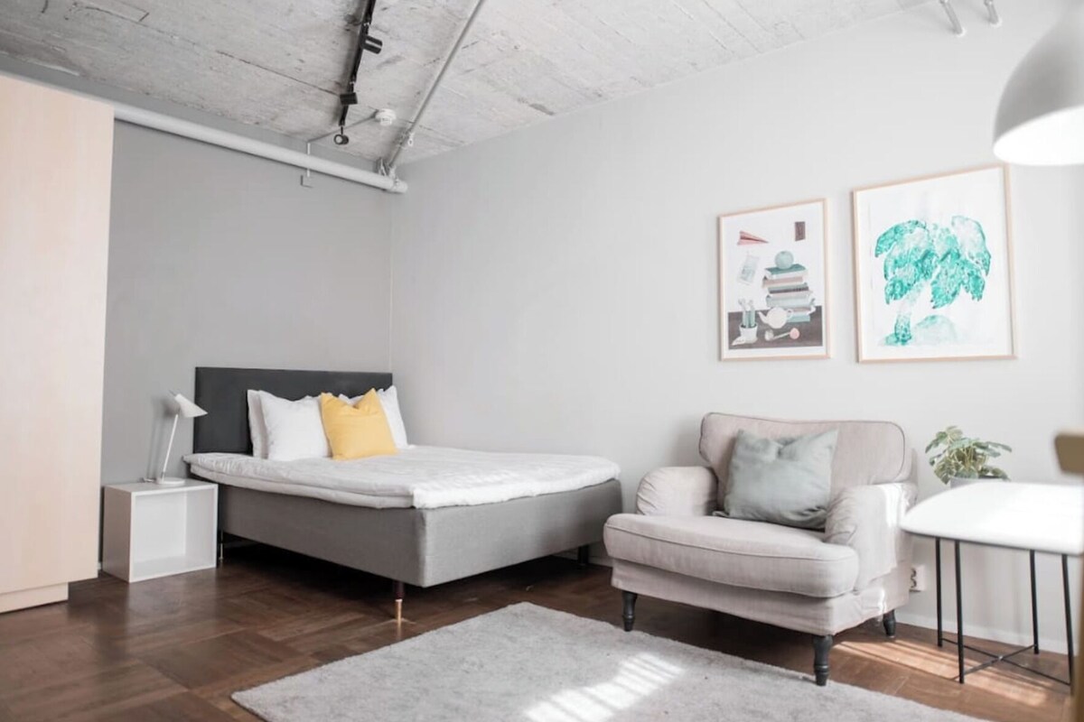 A modern bedroom with a bed, bedside table, chair, and artwork on the wall.