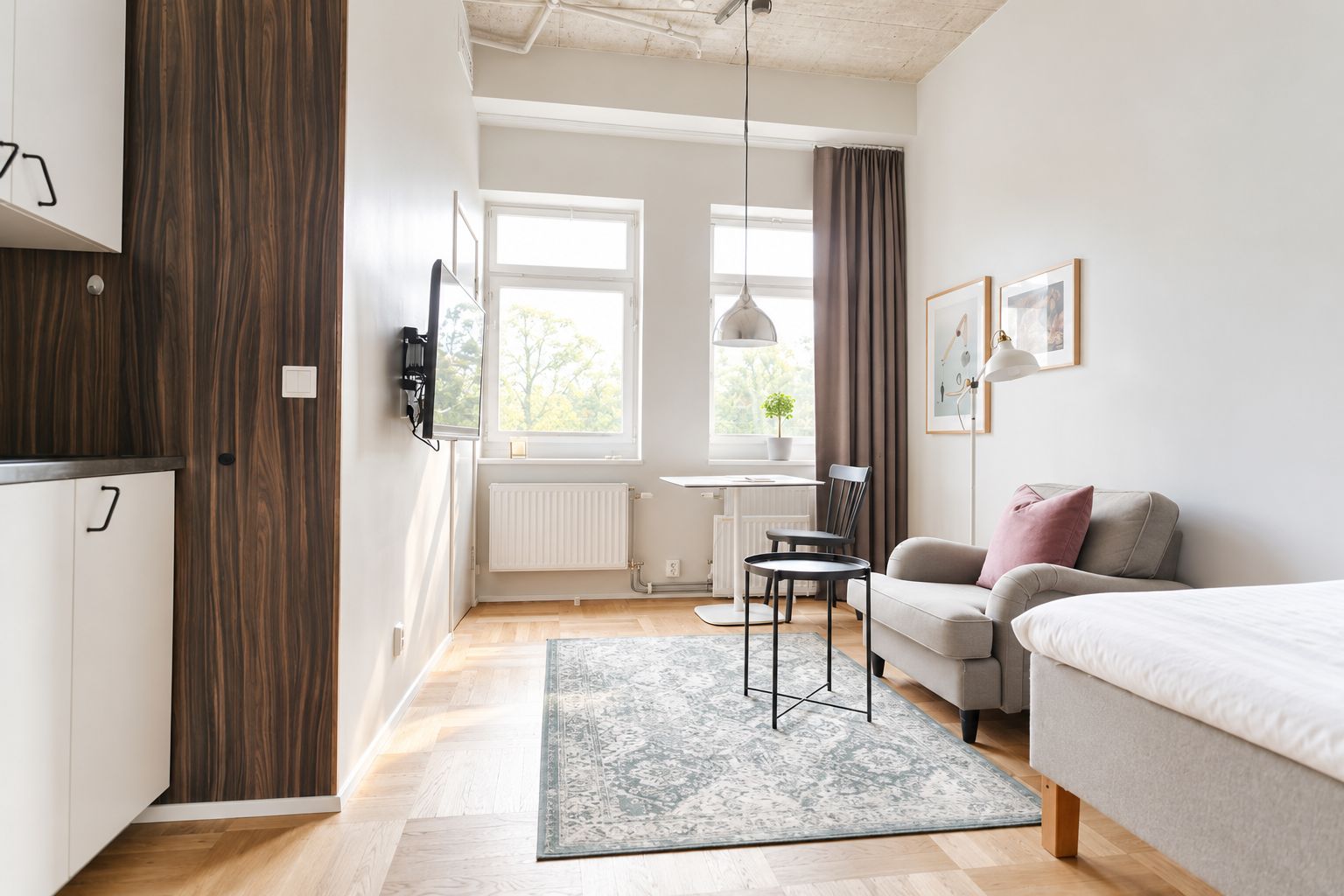 Une chambre moderne avec un lit, un bureau et une chaise. On y trouve une fenêtre avec des rideaux, un radiateur et une plante sur l’appui de fenêtre.