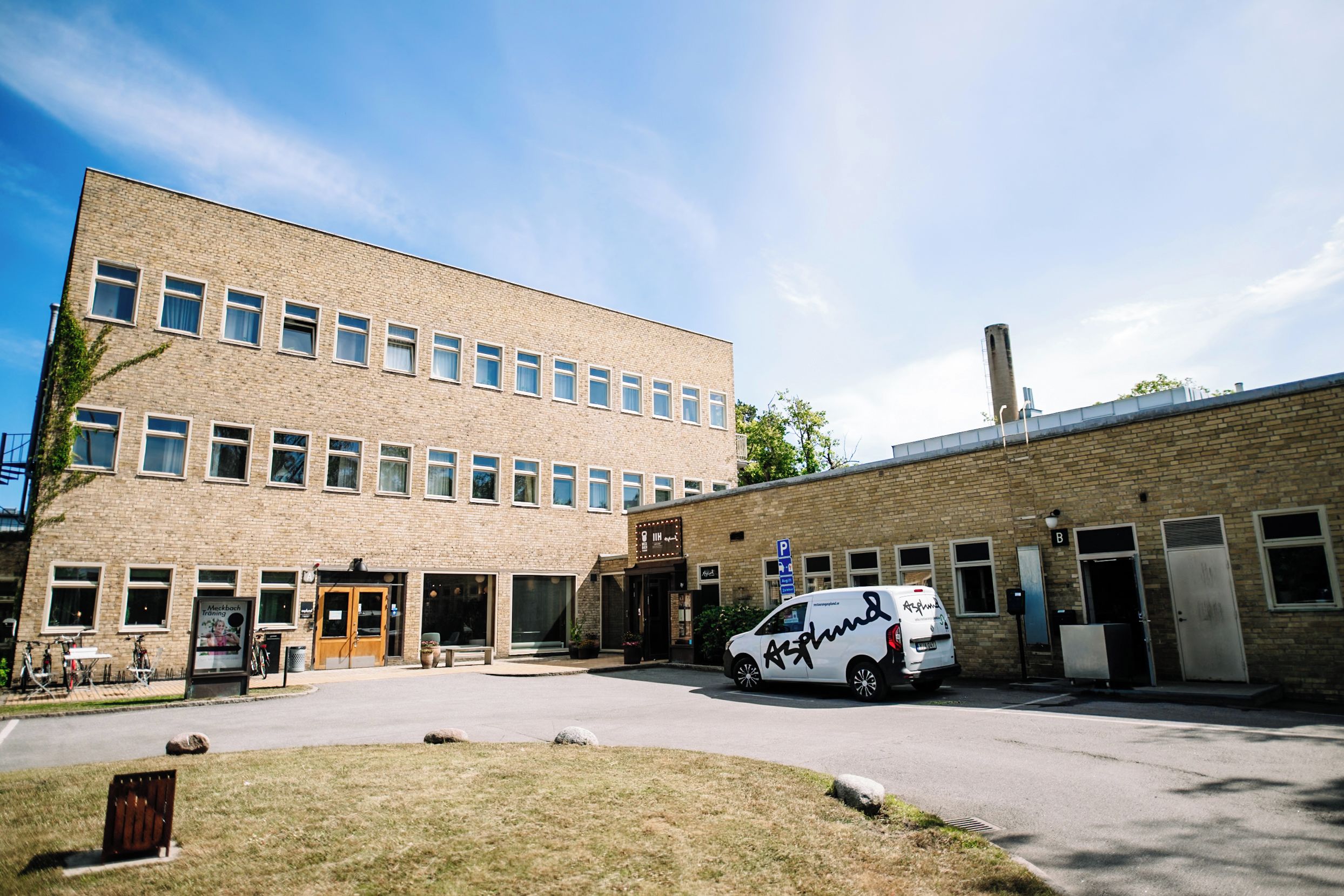 Un immeuble à plusieurs étages avec un espace de stationnement et un fourgon blanc garé devant.