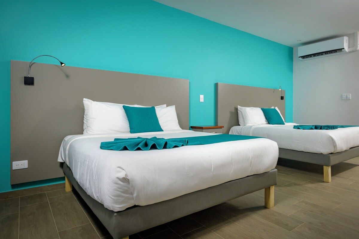 A hotel room with two beds, teal walls, and a modern design.