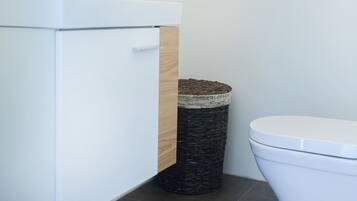 Une salle de bain moderne avec un lavabo blanc, un meuble en bois, une poubelle en osier et des toilettes blanches.