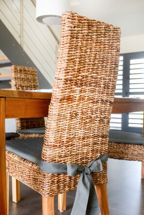 A wicker chair with a grey cushion and a grey ribbon tied around the backrest. - Belnem Villas (Kralendijk)