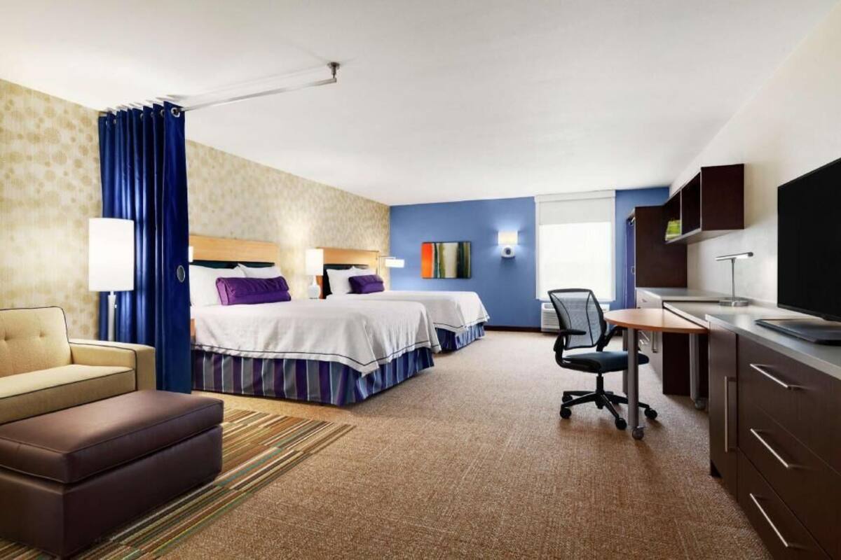 Habitació d'hotel amb dos llits, escriptori, cadira, televisió i finestra.