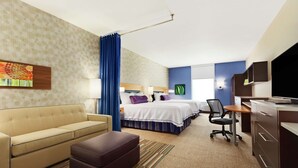 A hotel room with a sofa, a desk, a TV, a bed, and a chair.