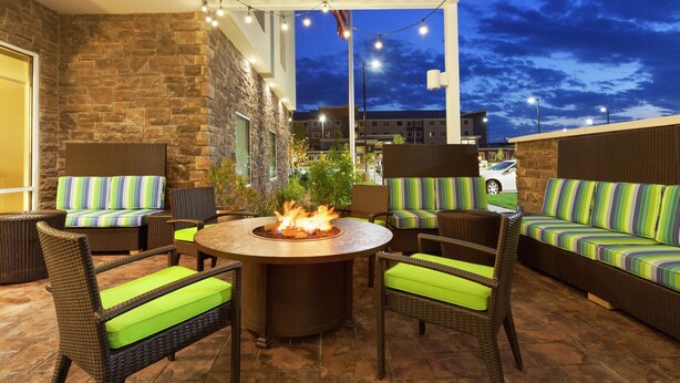 An outdoor patio area with wicker furniture, a central fire feature, and string lights.