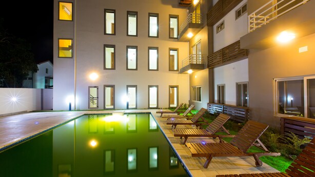 A modern building with a swimming pool, wooden lounge chairs, and a well-lit exterior. - Eagle's (Accra)