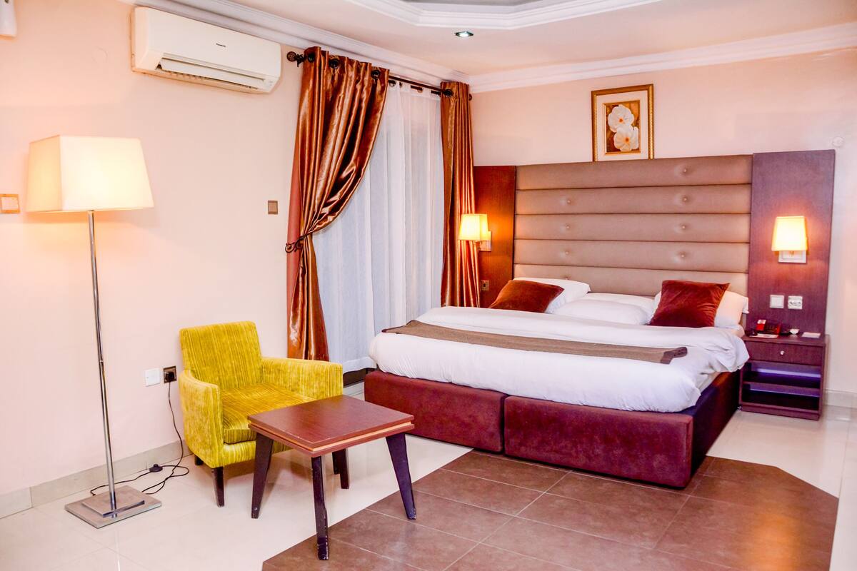 A hotel room with a bed, a chair, a table, and a lamp.