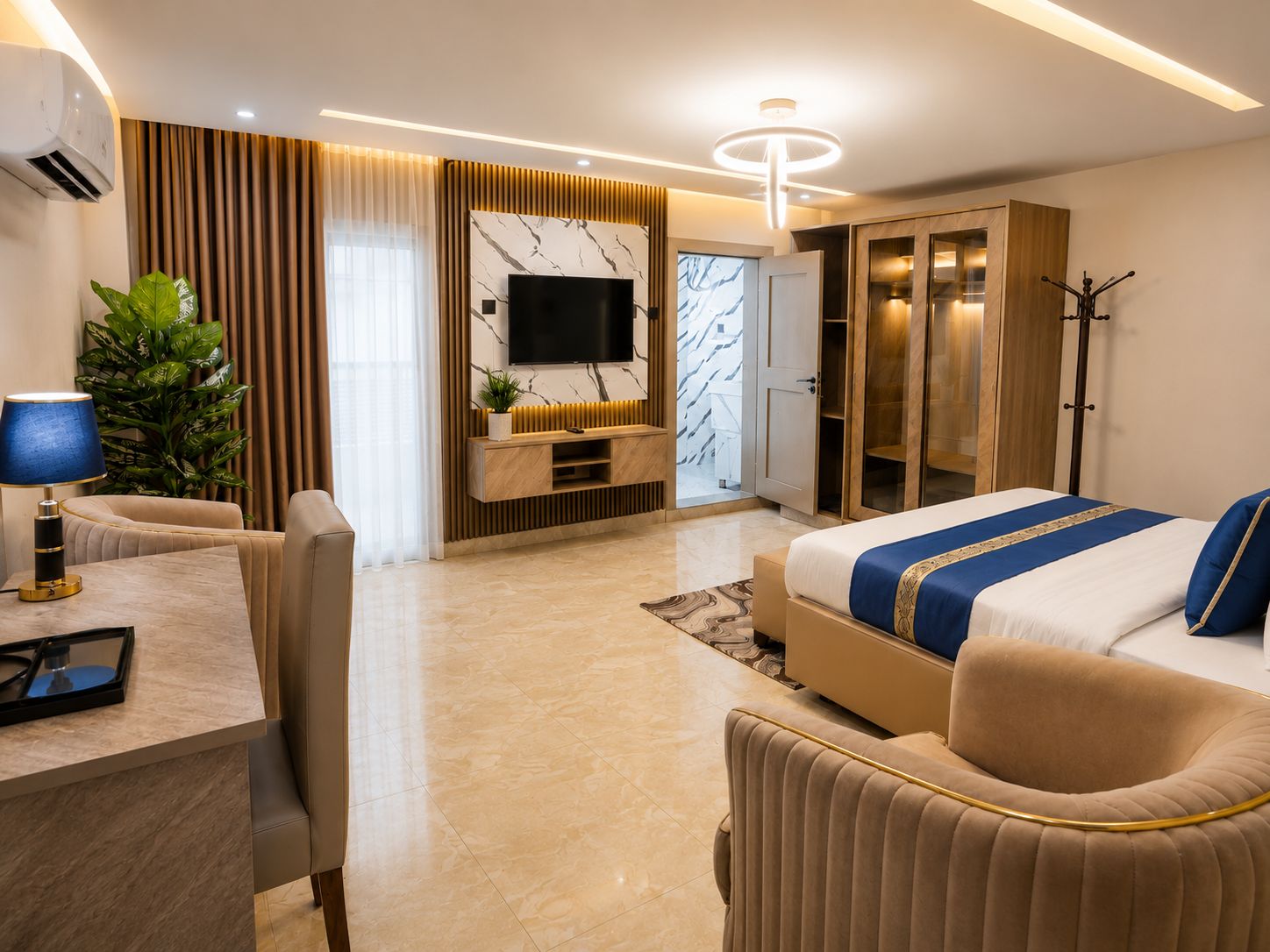 A modern hotel room with a bed, seating area, TV, wardrobe, and a plant.