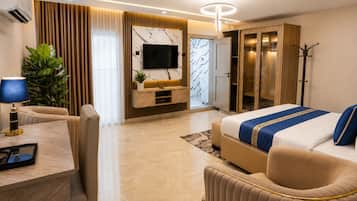 A modern hotel room with a bed, seating area, TV, wardrobe, and a plant.
