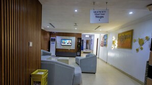 A lobby with seating areas, a television screen, and a sign instructing to mind your steps. - GolfView Suites & Conference Center (Lagos)
