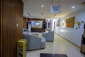 A lobby with seating areas, a television screen, and a sign instructing to mind your steps.