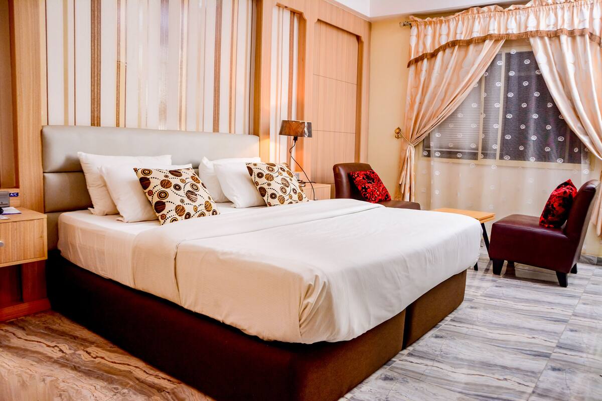 A hotel room with a large bed, a desk, a chair, and a window with curtains.