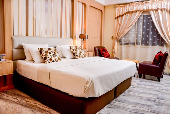 Habitación de hotel con una cama grande, un escritorio, una silla y una ventana con cortinas.