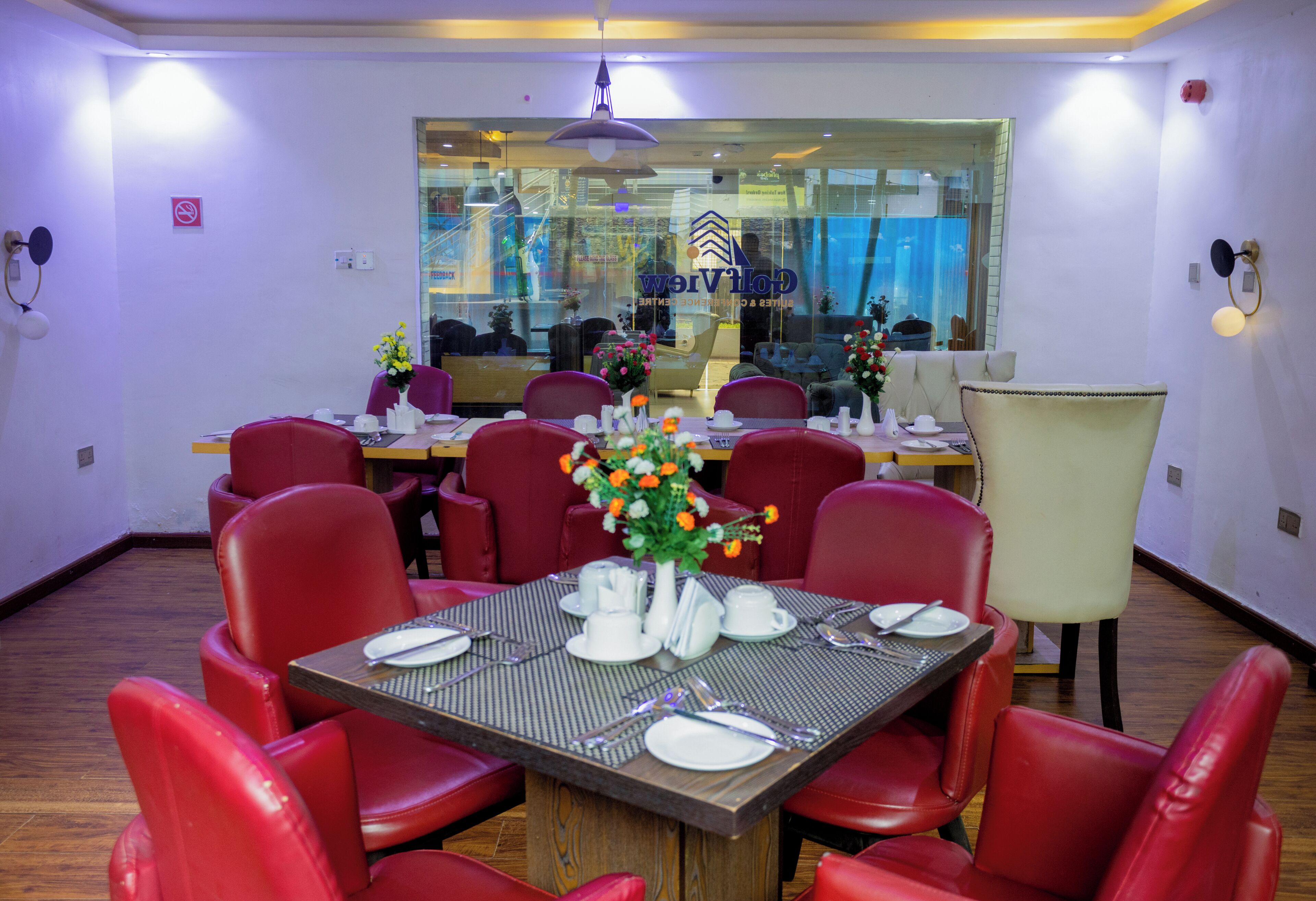 A dining area with red chairs, a table set for four, and a large window with a reflection of the interior.