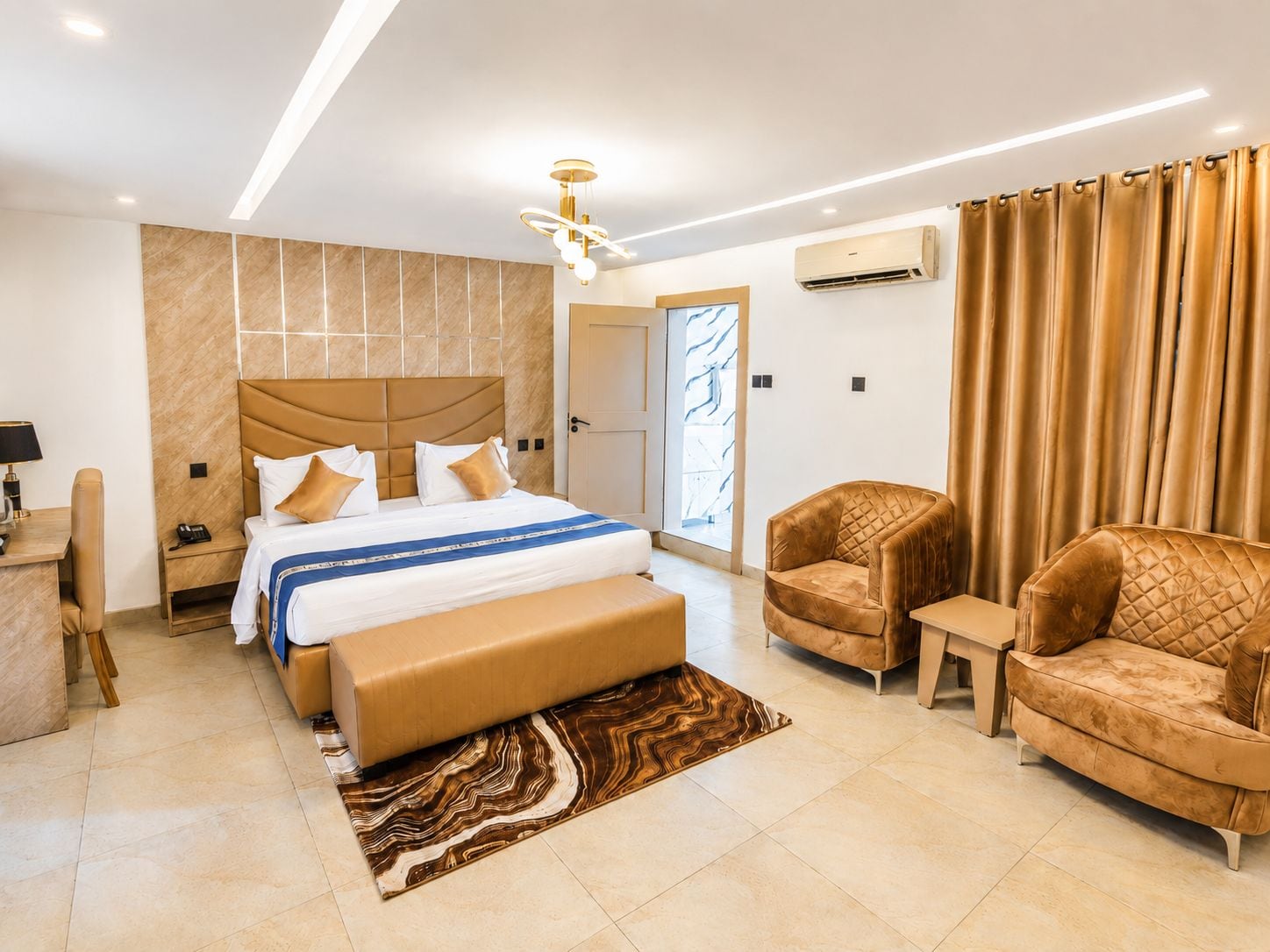 A modern hotel room with a large bed, a desk, a chair, and a sofa.