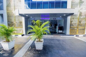 A reception area with a sign indicating 'RECEPTION' and 'IN' and 'OUT' directions. There are potted plants in front of the entrance. - GolfView Suites & Conference Center (Lagos)