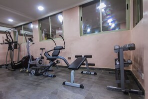 Ein Fitnessraum mit Trainingsgeräten, darunter Laufband, Crosstrainer und eine Gewichtbank.