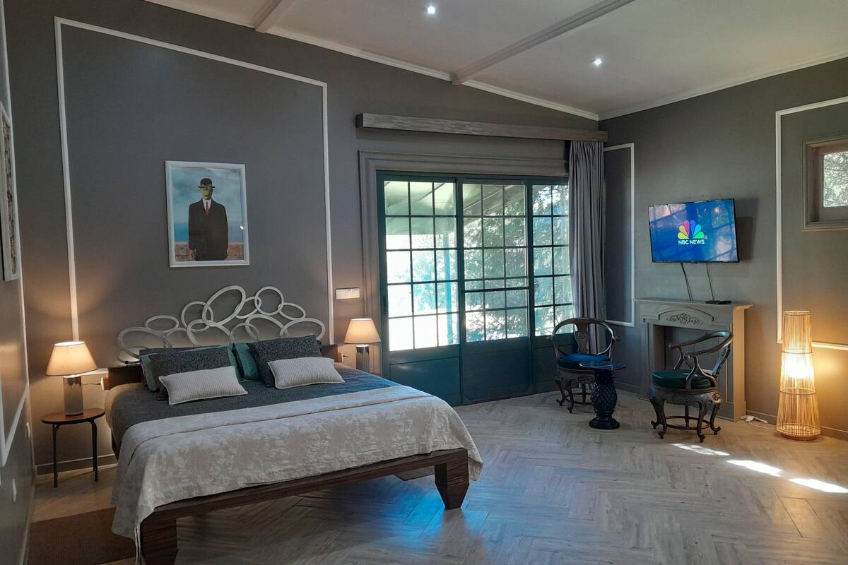 A bedroom with a bed, bedside lamps, a TV, a chair, and a window with curtains.