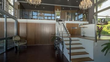 A spacious interior with a grand staircase, large windows, and a chandelier.