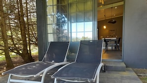 Two lounge chairs outside a building with a glass door, a dining area visible inside, and trees in the background. - Gala Da Vittoria (Ponta Delgada)