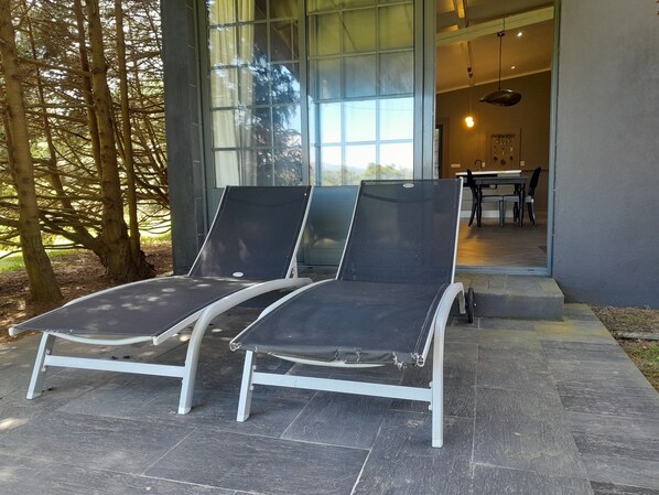 Two lounge chairs outside a building with a glass door, a dining area visible inside, and trees in the background. - Gala Da Vittoria (Ponta Delgada)