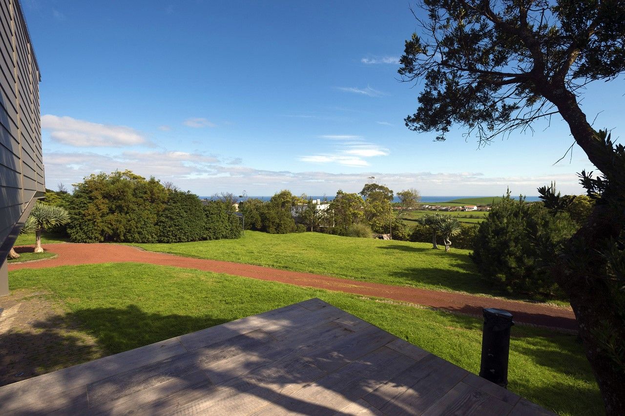A view from a balcony overlooking a green lawn with a red path, trees, and a distant landscape.