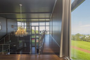 A spacious interior with a grand staircase, a chandelier, and a view of a lush green landscape through large windows. - Gala Da Vittoria (Ponta Delgada)