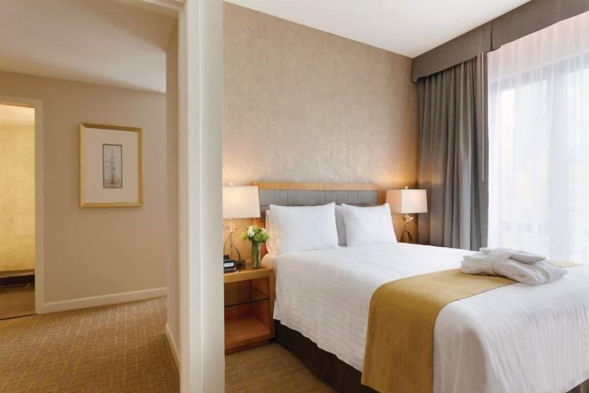 Hotelkamer met een bed, twee bedlampen, een nachtkastje met een bloevas en een lijst aan de muur.