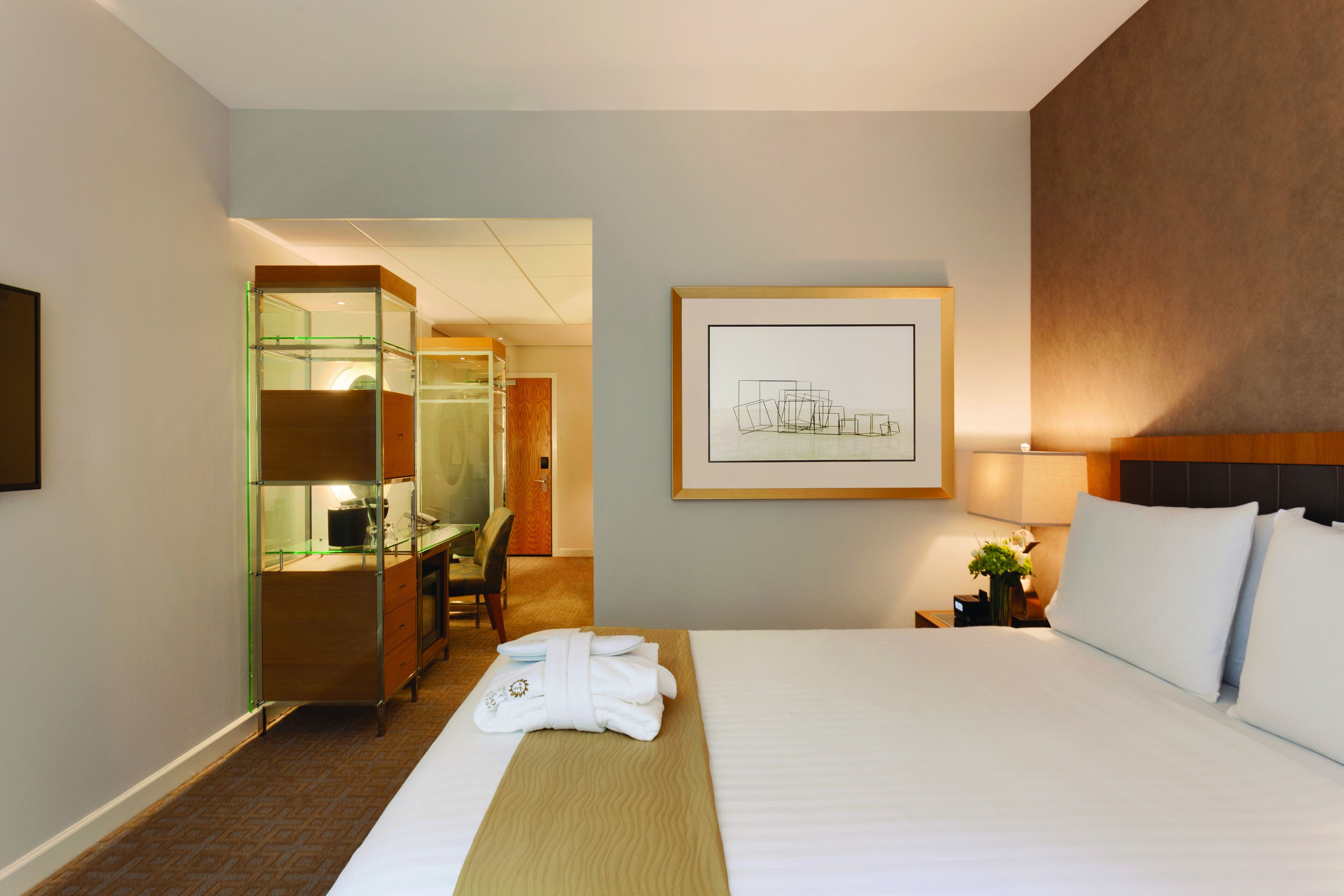 Habitación de hotel con cama, escritorio, silla y baño visible a través de una puerta de vidrio.