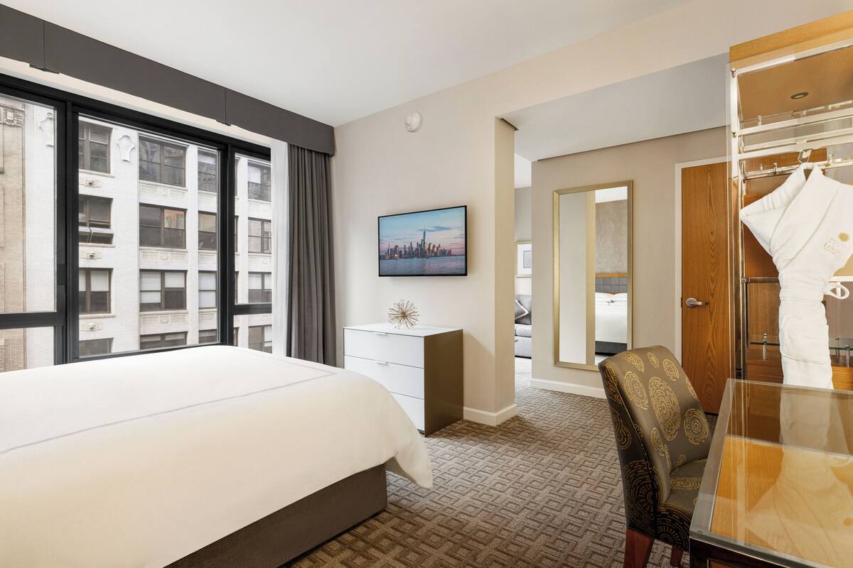 Une chambre d’hôtel avec un grand lit, un bureau, une chaise, une armoire et un tableau représentant un paysage urbain accroché au mur.