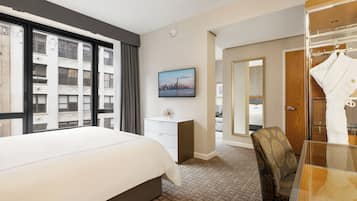 Ein Hotelzimmer mit einem großen Bett, einem Schreibtisch, einem Sessel, einem Kleiderschrank und einem Stadtbild an der Wand.