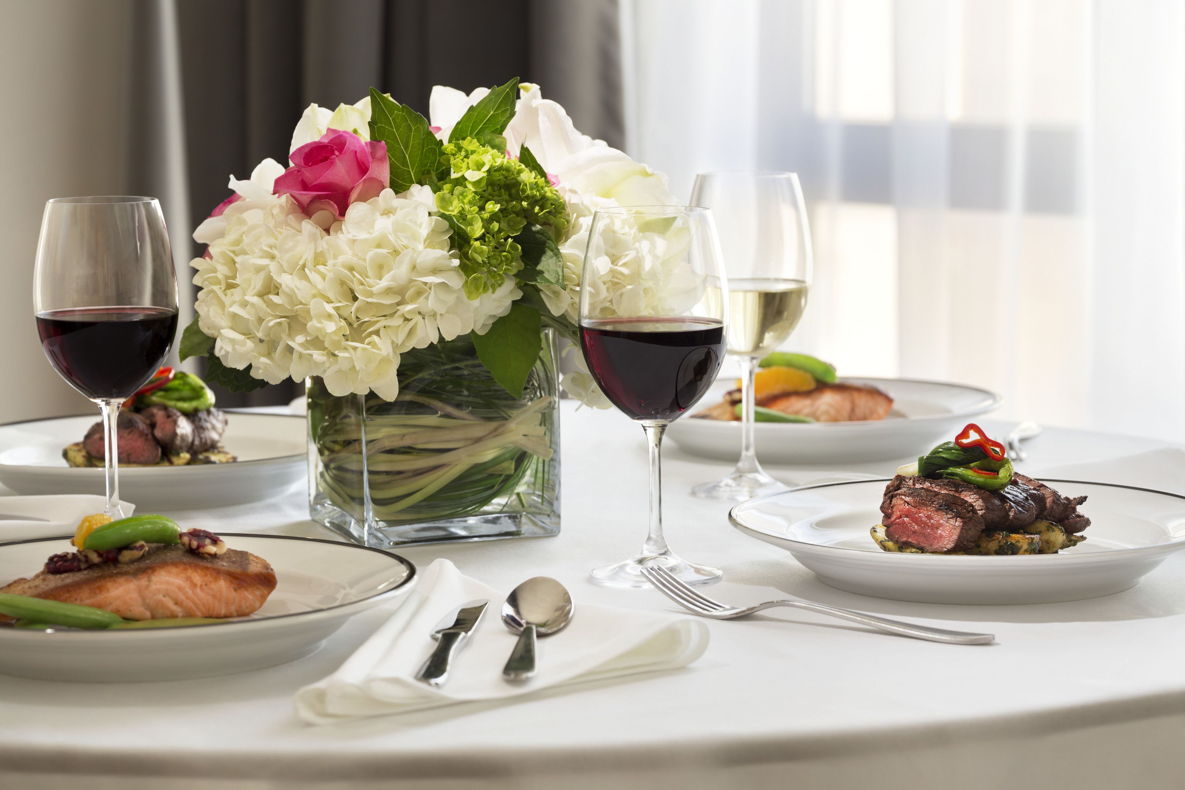 Una mesa de comedor con platos de comida, copas de vino y un jarrón de flores.
