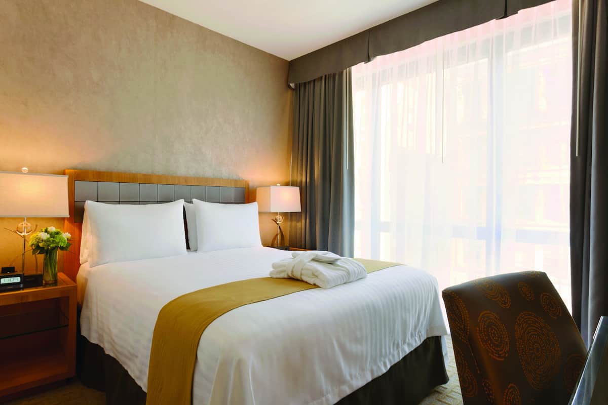 Une chambre d’hôtel avec un grand lit, une table de chevet avec une lampe, une chaise et une fenêtre avec des rideaux.