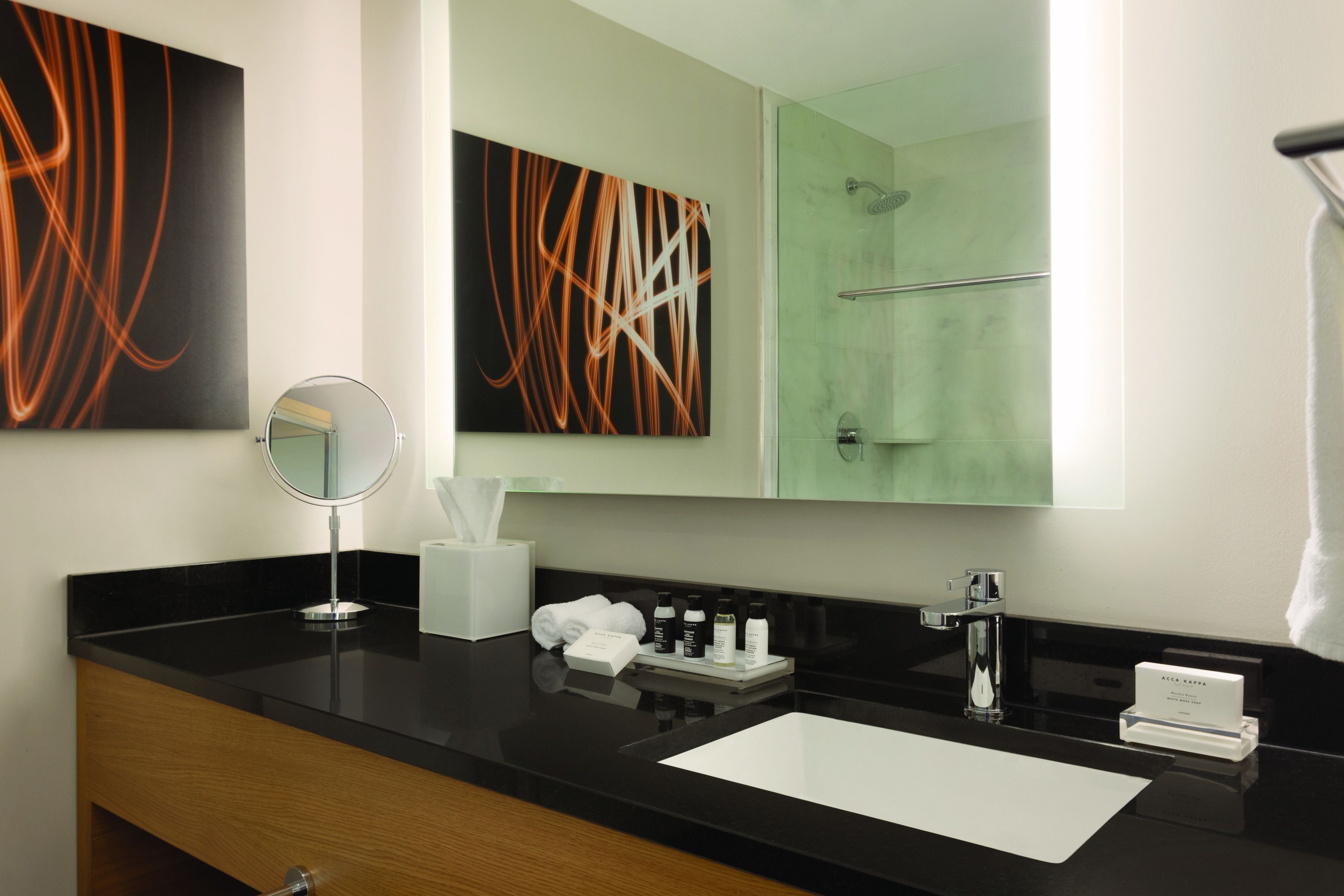A modern bathroom with a black countertop, a round mirror, a white sink, and a glass shower enclosure.