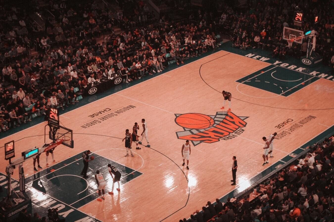 Een basketbalveld met een groot teamlogo, een scorebord en een menigte toeschouwers.