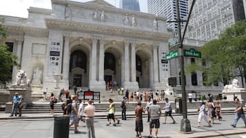 A historic building with classical architecture, including columns and statues, located at a busy intersection.