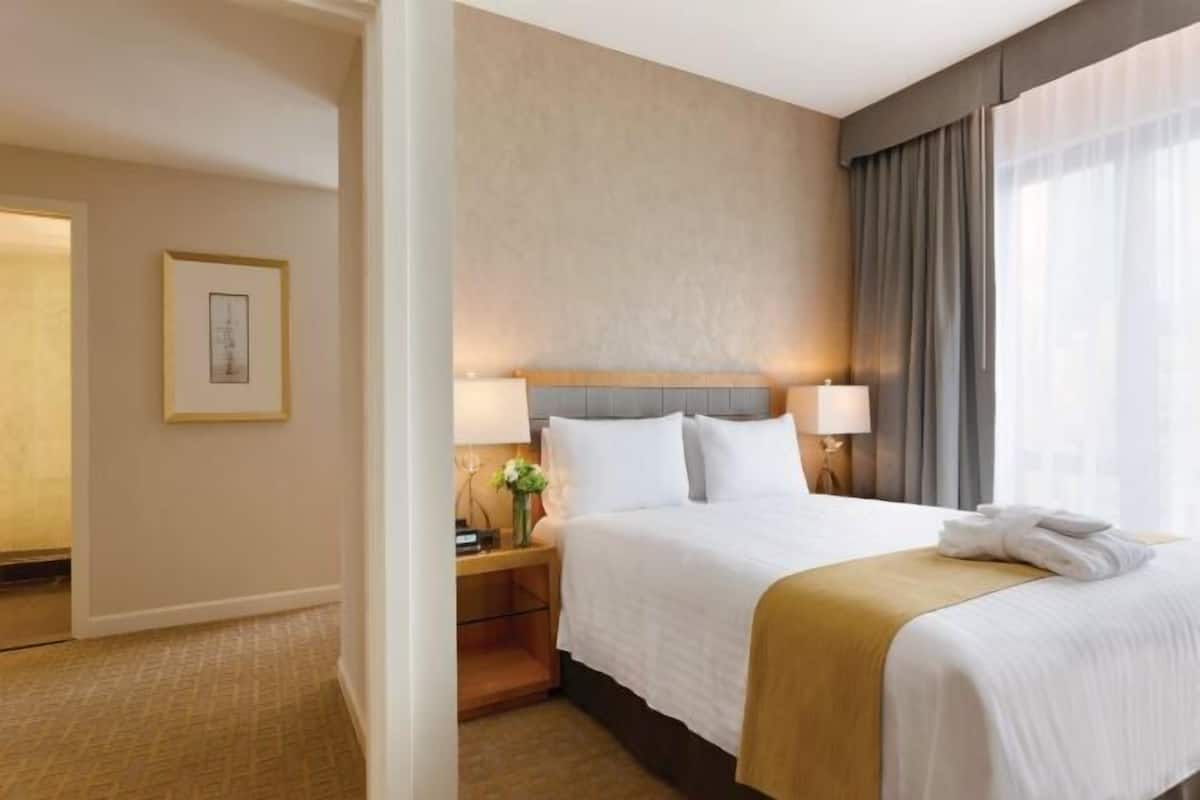 Ein Hotelzimmer mit einem Bett, zwei Nachttischlampen, einem Nachttisch mit Blumen und einem gerahmten Bild an der Wand.
