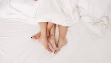 A bed with white linens and a person lying on it.