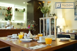 Una escena de desayuno con una mesa de madera, platos, tazas y un jarrón con flores.