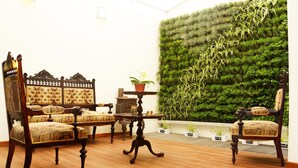 Una habitación con una silla y mesa de madera tradicionales, un jardín vertical de color verde y una pequeña planta en maceta sobre una mesita.