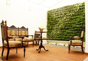 Una habitación con una silla y mesa de madera tradicionales, un jardín vertical de color verde y una pequeña planta en maceta sobre una mesita.