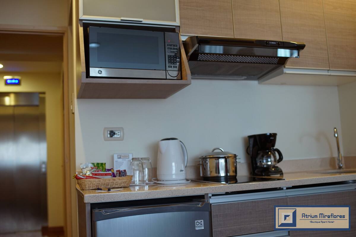 Uma cozinha compacta com micro-ondas, cafeteira e chaleira sobre o balcão.