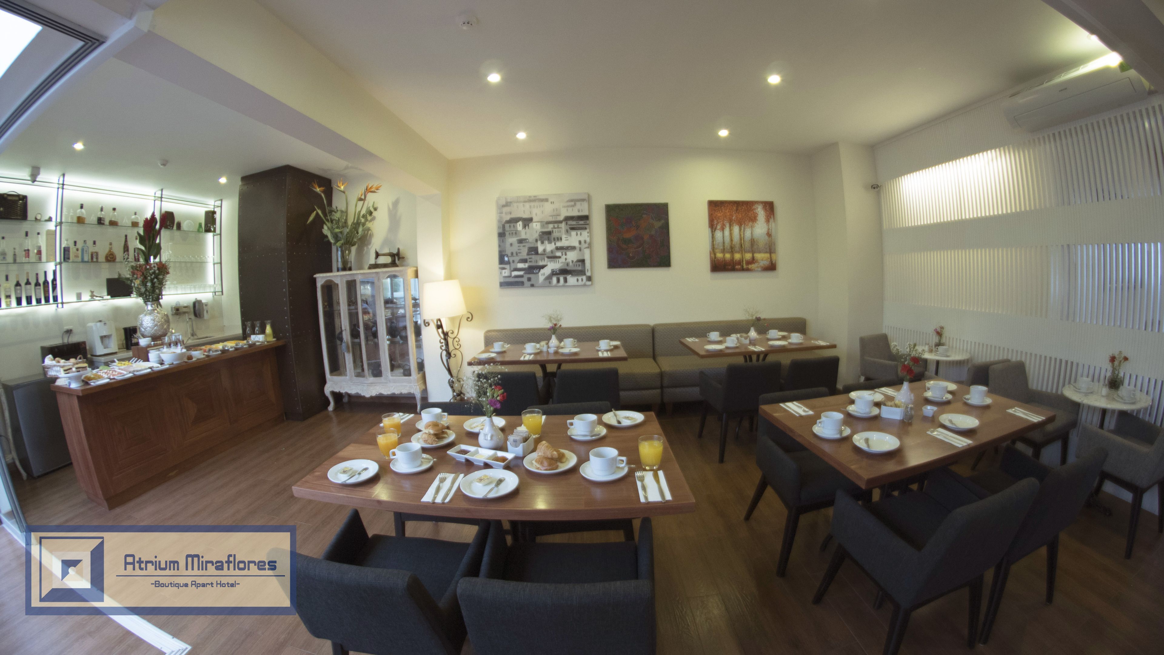 Un comedor con varias mesas dispuestas para el desayuno, una barra con distintos tipos de botellas y un mueble decorativo.