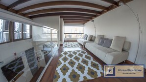 Un salón moderno con un sofá, un tapiz estampado y un balcón con vistas a la ciudad.