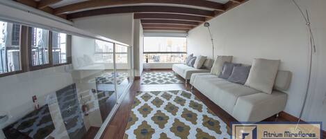 Un salón moderno con un sofá, un tapiz estampado y un balcón con vistas a la ciudad.