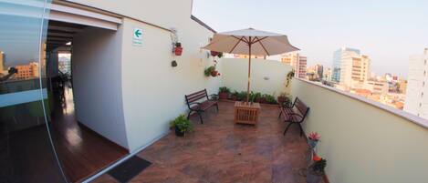 A balcony with a bench, an umbrella, and potted plants.