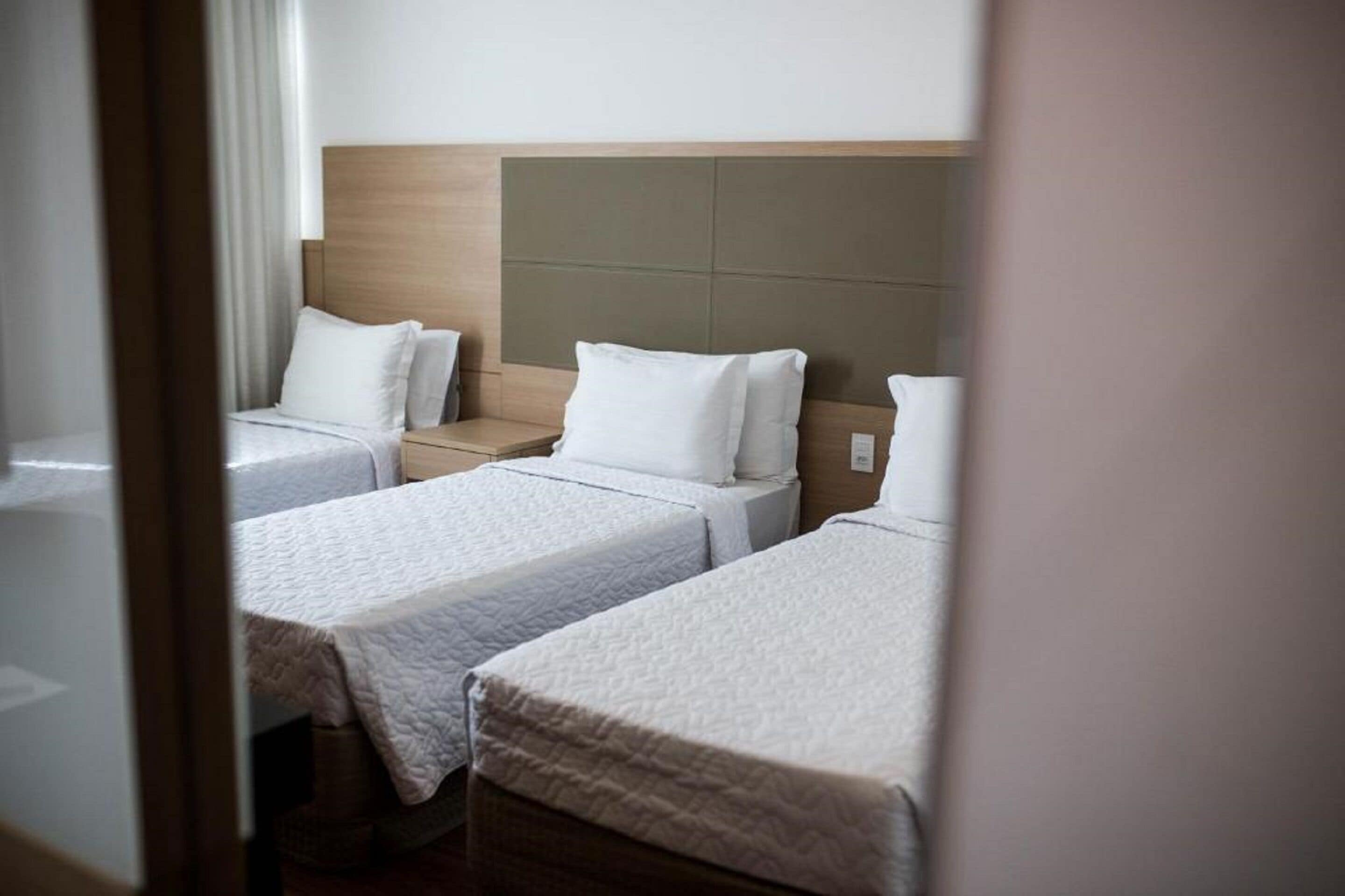 A hotel room with three single beds, each with a wooden headboard and white bedding.
